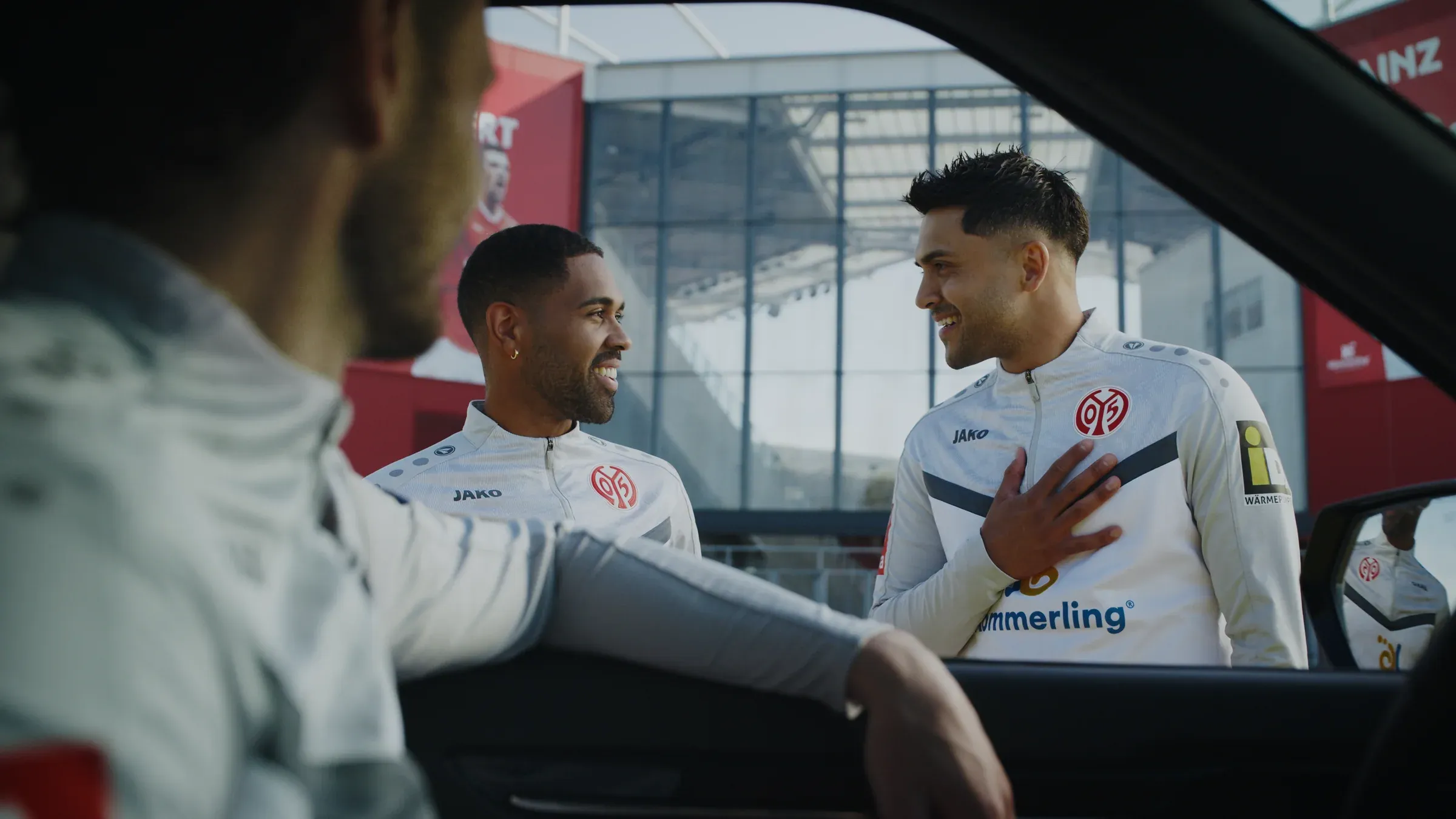 Ein Spieler von Mainz 05 lädt vor dem Stadion neben einem gelben iDM-Fahrzeug ein gebrandetes Requisit aus
